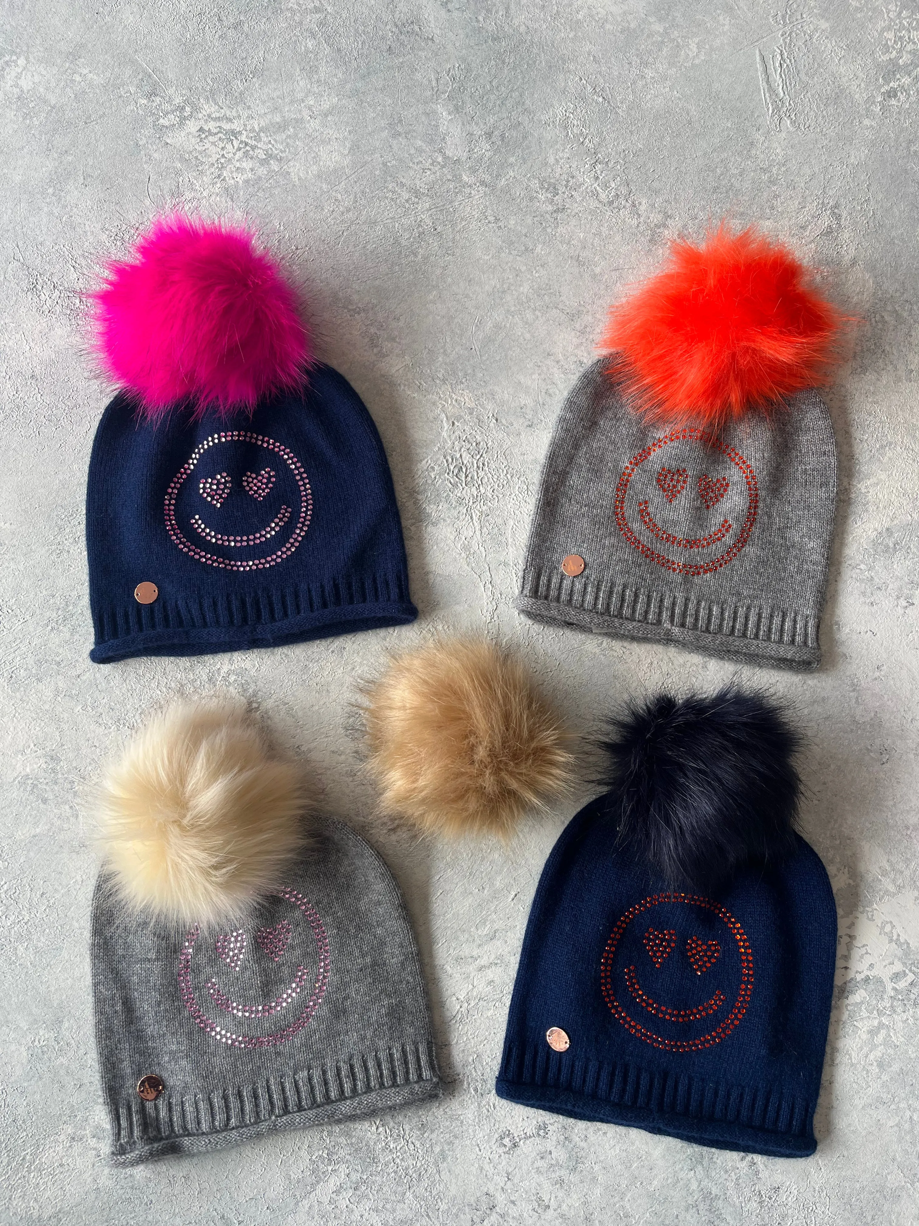 Navy cashmere plain knit beanie with a pink smiley embellishment & faux fur pom